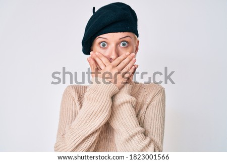 Young blonde woman wearing french look with beret shocked covering mouth with hands for mistake. secret concept. 