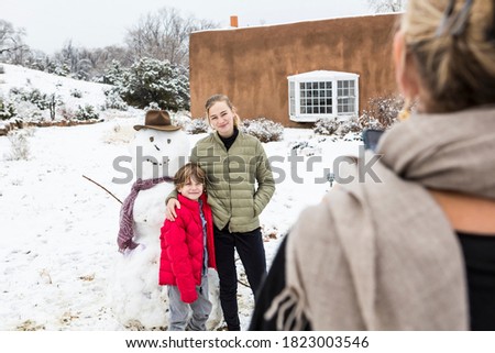 mother taking portrait of her children with snowman in background