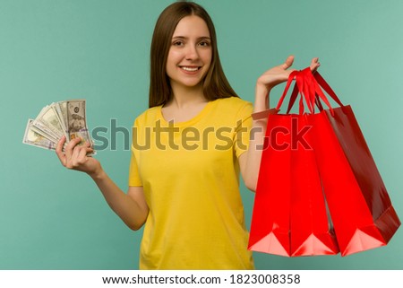 Photo of cheerful young woman holding fan of money and red shopping bags,isolated on blue background - image