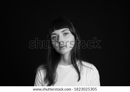 Studio portrait of a pretty brunette woman in a white blank t-shirt, against a plain black background, looking at camera Royalty-Free Stock Photo #1823025305