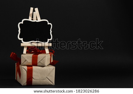 Gift with red ribbon and frame plaque on black background, layout for design. Copy space.