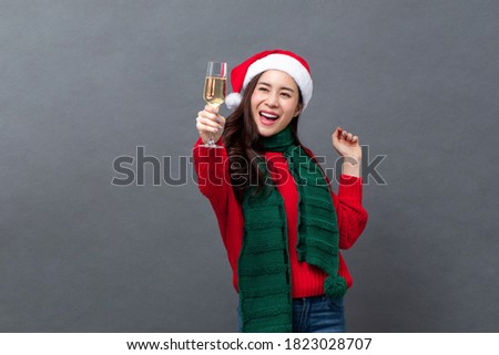 Happy Asian woman in colorful red and green clothes drinking champagne celebrating Christmas in gray isolated background