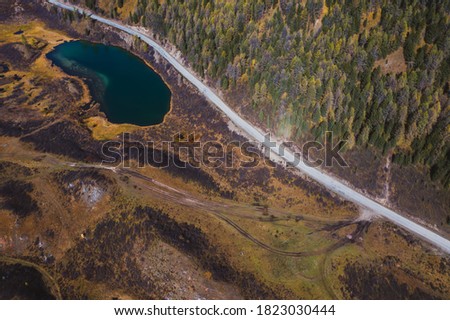 Road in tundra area with fur colourful autumn forest and mountain lake. Aerial drone view 