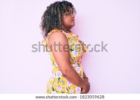 Young african american plus size woman wearing casual clothes looking to side, relax profile pose with natural face with confident smile. 