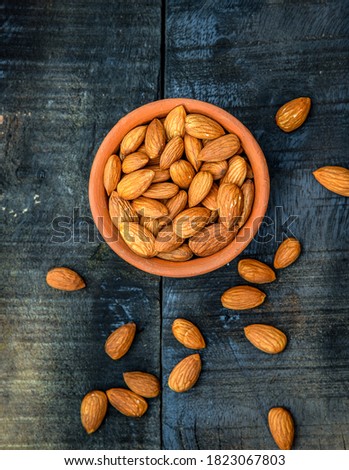 Top view of almonds on dark stone table with wood spoon or scoop. Almond in wooden bowl. Nuts freely laid on dark board. 