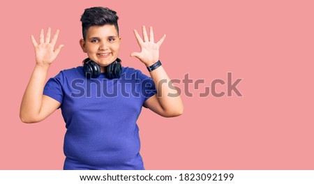 Little boy kid listening to music wearing headphones showing and pointing up with fingers number ten while smiling confident and happy. 