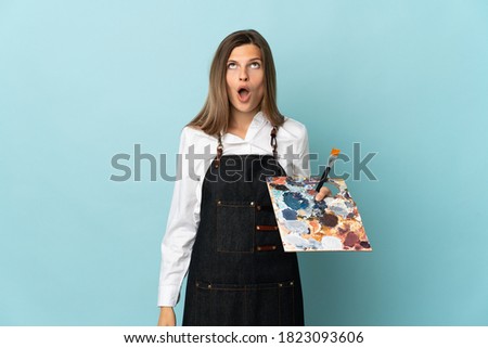 Young artist Slovak woman isolated on blue background looking up and with surprised expression