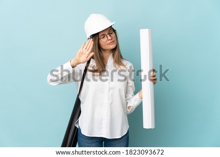 Slovak architect girl holding blueprints isolated on blue background making stop gesture and disappointed