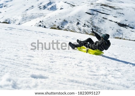 A young Caucasian boy playing with a sled on the mountain covered with snow