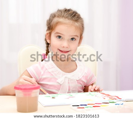 Cute smiling little girl child drawing with paint and paintbrush at home