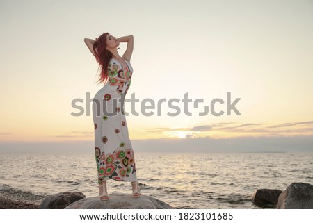 young slim girl in a dress posing at sunset on the sea