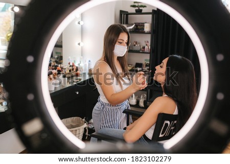 Female makeup master in protective medical. Beautiful model in beauty studio. Professional make up artist apply lipstick. Makeup in qurantine