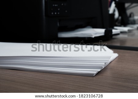 Workspace with a blank paper on a wooden table next to a printer machine, selective focus, copy space