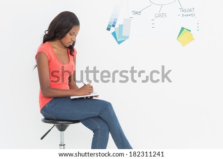 Designer sitting and writing in front of whiteboard in creative office