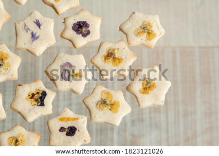 Star shaped biscuits decorated with edible flowers, pansies and cornflower petals. Photographed on a wooden background.