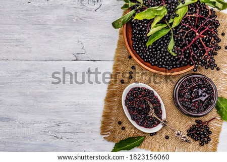Elderberry jam. Ripe berries, sweet and healthy dessert. Alternative medicine and lifestyle. White wooden boards background, top view Royalty-Free Stock Photo #1823156060