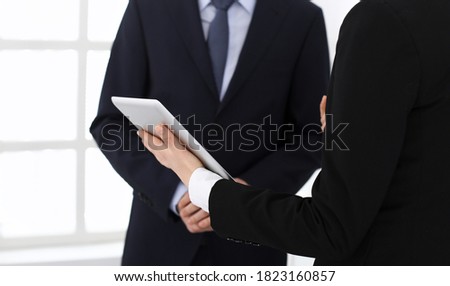 Businessman and woman using tablet computer for discussing questions in office. Partners or colleagues at meeting. Business cooperation concept
