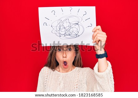 Young beautiful blonde woman holding picture of chaos above head scared and amazed with open mouth for surprise, disbelief face 