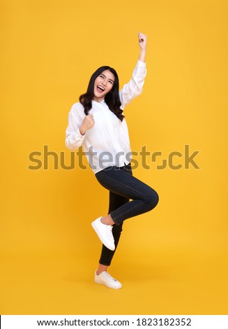 Happy Asian woman smiling and standing with hand up celebrating gesture on yellow background. Royalty-Free Stock Photo #1823182352