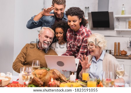 Selective focus of multicultural family having video call on laptop near food during thanksgiving
