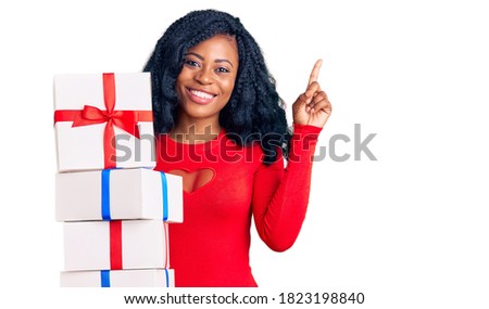 Beautiful african american woman holding presents surprised with an idea or question pointing finger with happy face, number one 