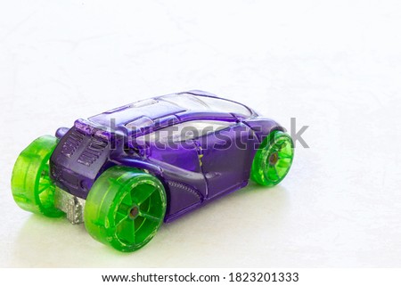 An old and shabby purple children's toy stroller with green tires isolated on a white marble background. Miniature car. Used toy.