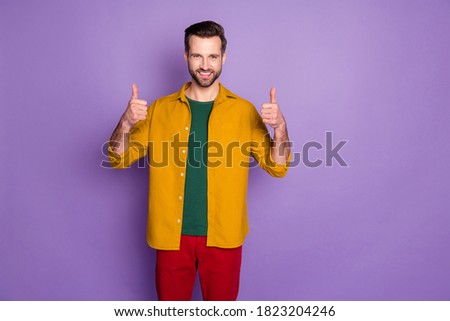 Photo of attractive handsome guy raise thumb fingers up overjoyed open mouth expressing agreement approval wear casual yellow shirt red pants isolated purple color background