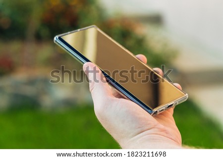 Cropped shot of male hands holding smartphone with blank screen copy space for your text message or informational content, reading text message on cell phone against green nature background