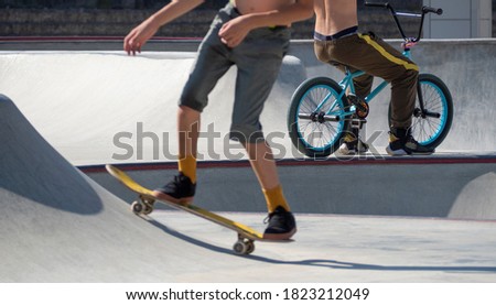 Young active teenagers riding stunts on skateboard and BMX bike in skatepark