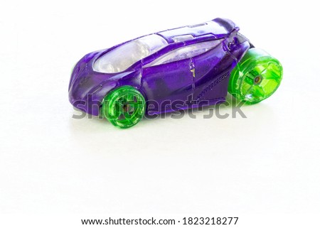 An old and shabby purple children's toy stroller with green tires isolated on a white marble background. Miniature car. Used toy.