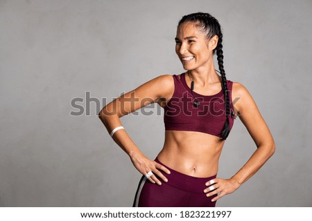 Happy beautiful fit woman laughing and looking away after gym exercise isolated on grey background. Middle aged woman wearing sports bra on gray wall with copy space. Carefree fitness girl resting. Royalty-Free Stock Photo #1823221997