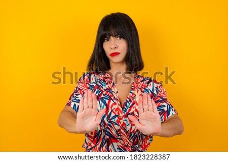Young woman with retro short hair wearing casual clothes standing over isolated yellow background Moving away hands palms showing refusal and denial with afraid and disgusting expression. Stop
