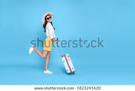 Happy young Asian tourist woman holding passport and boarding pass with baggage going to travel on holidays isolated on blue background. Royalty-Free Stock Photo #1823241620