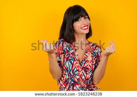 Photo of beautiful young woman wearing Hawaiian shirt over yellow wall making money gesture.