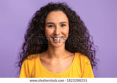 Happy Person. Portrait of smiling young friendly woman with tanned skin and beautiful curly hair looking at camera, posing in studio, isolated over purple background, closeup shot with copy space Royalty-Free Stock Photo #1823288255
