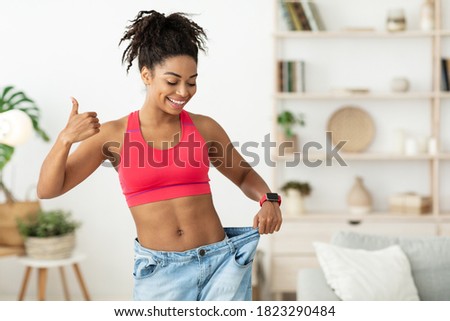 Happy African Lady Showing Result Of Successful Weight Loss Gesturing Thumbs-Up, Wearing Old Oversize Jeans Standing At Home. Slimming Motivation And Dieting Concept. Blank Space For Text Royalty-Free Stock Photo #1823290484