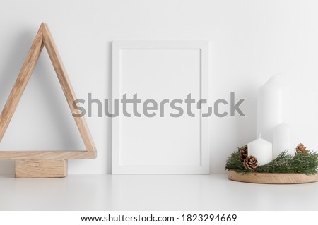 White frame mockup with a wooden tree and candles on a white table. Christmas decoration.