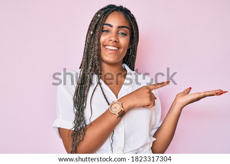 Young african american woman with braids wearing casual summer shirt amazed and smiling to the camera while presenting with hand and pointing with finger. 