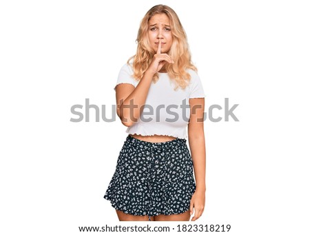 Young blonde girl wearing casual white tshirt asking to be quiet with finger on lips. silence and secret concept. 