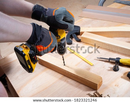 Man hands is drilling the wooden bar with cordless drill. Tools around. Repairs. Close up.  Royalty-Free Stock Photo #1823321246