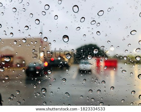 Rain drops on glass with a view of cars in a parking lot on a rainy summer day.