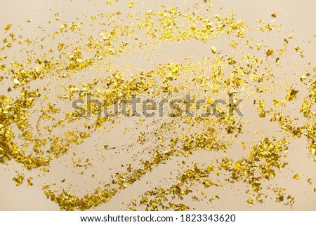 Golden confetti on beige paper trendy background. Festive holiday backdrop. Birthday congratulations Christmas New Year. Flat lay, top view, copy space.