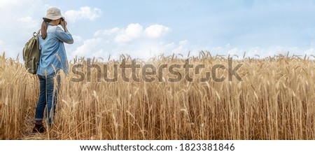 Asian young woman with backpack taking a photo in barley field on summer. Travel and Vacation concept.