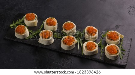 Snack. Red caviar in pita roll with arugula on a black background. Background image, copy space