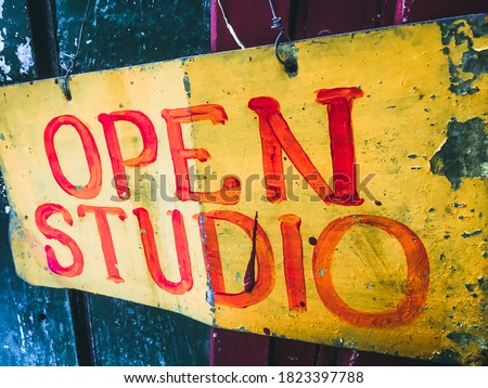 Yellow vintage metal sign hanging on a door that reads the phrase Open Studio written in red letters in the city of Havana, Cuba.