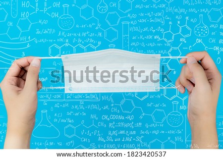Young man hands holding white respirator mask for mouth and nose covering. Pastel blue background. Protection in dangerous virus time. Healthcare concept. Closeup. Point of view shot. Top down view.