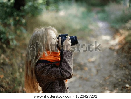 European girl child takes pictures on camera in autumn park. Fall.
