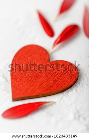 Red retro wooden heart and gerbera daisy petals on stone white background. Love concept, romantic or valentines day card mockup with copy space.