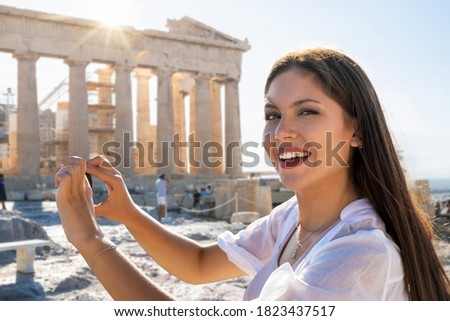 Portrait of a pretty tourist woman takes pictures of the Parthenon Temple at the Actropolis of Athens, Greece, during a sightseeing trip