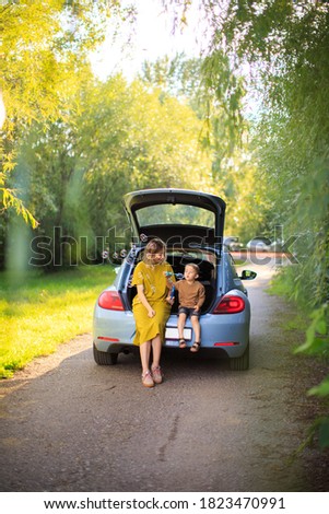 Beautiful mother and little son travelers sit in trunk of car on road and blow soap bubbles. Photo about family travel